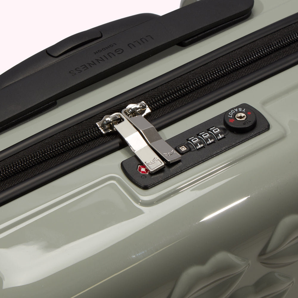 Close-up of a sage green Lulu Guinness suitcase showing the TSA-approved combination lock and zipper.
