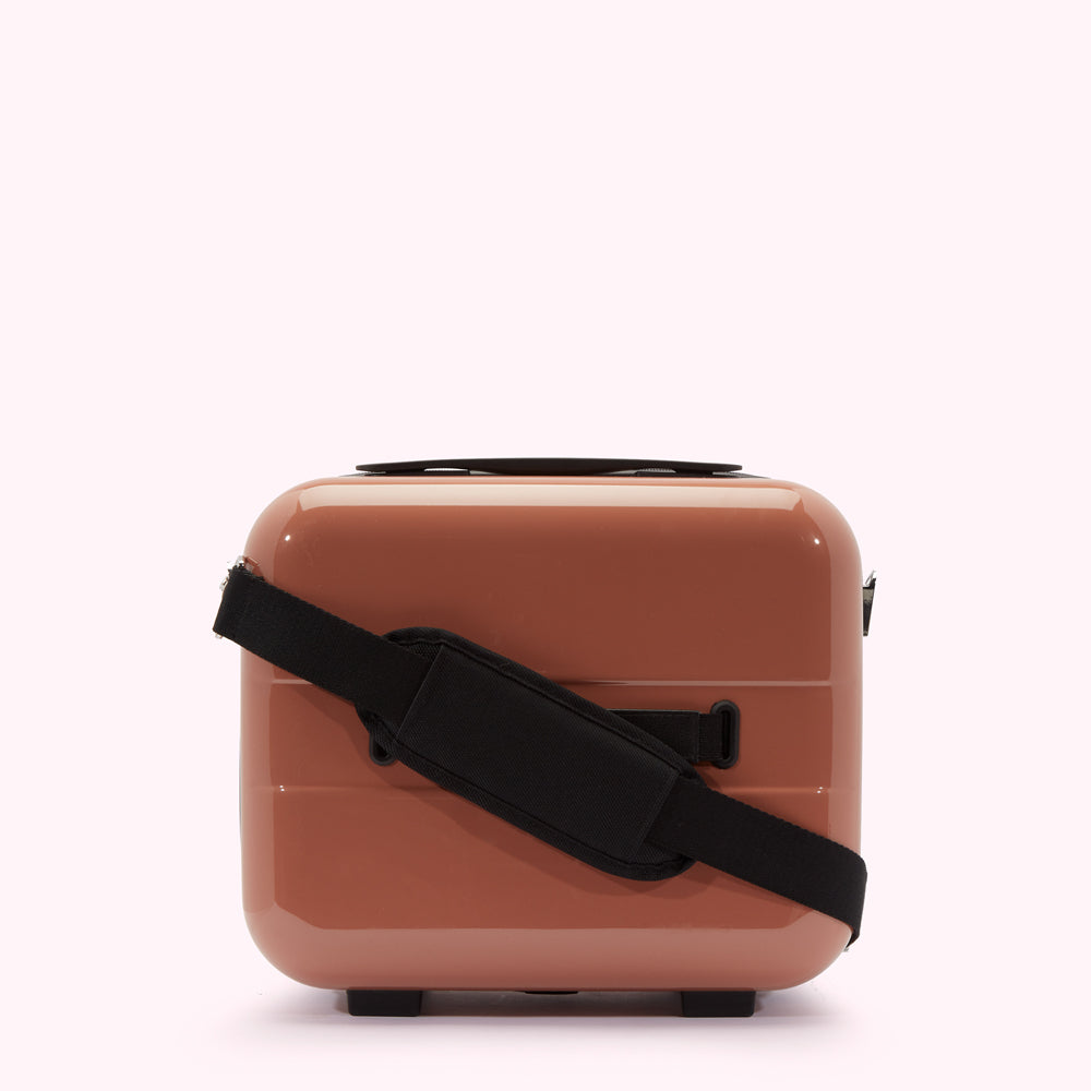 Dusty rose-coloured carry-on suitcase with a black shoulder strap.
