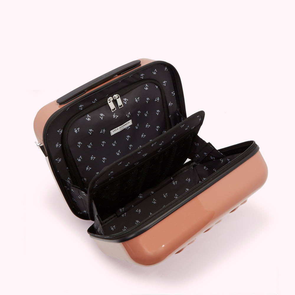 Open rose-gold Lulu Guinness suitcase with black patterned lining showing various compartments.
