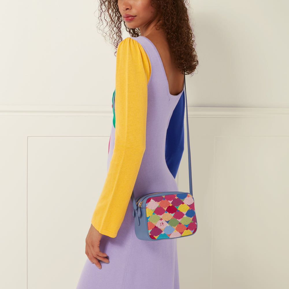 Woman wearing a lavender and yellow dress with a small blue crossbody bag featuring a colourful embroidered pattern.
