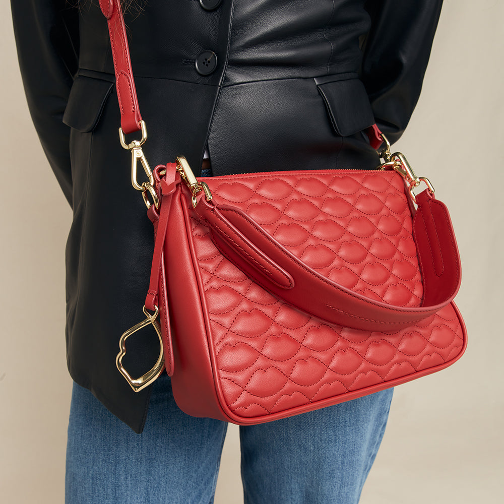 Red quilted handbag with gold accents held by a person wearing a black coat and blue jeans.