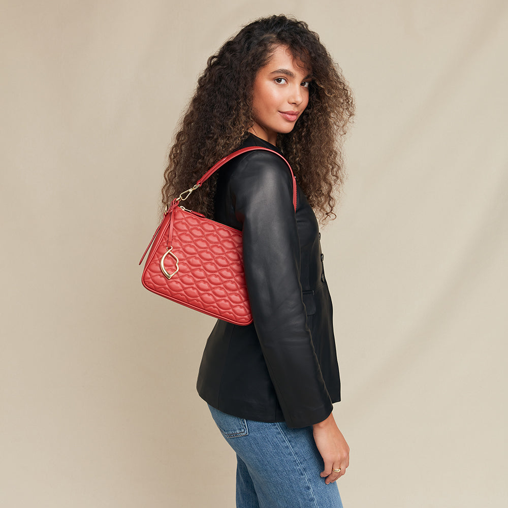 Woman holding a red quilted handbag against a beige background