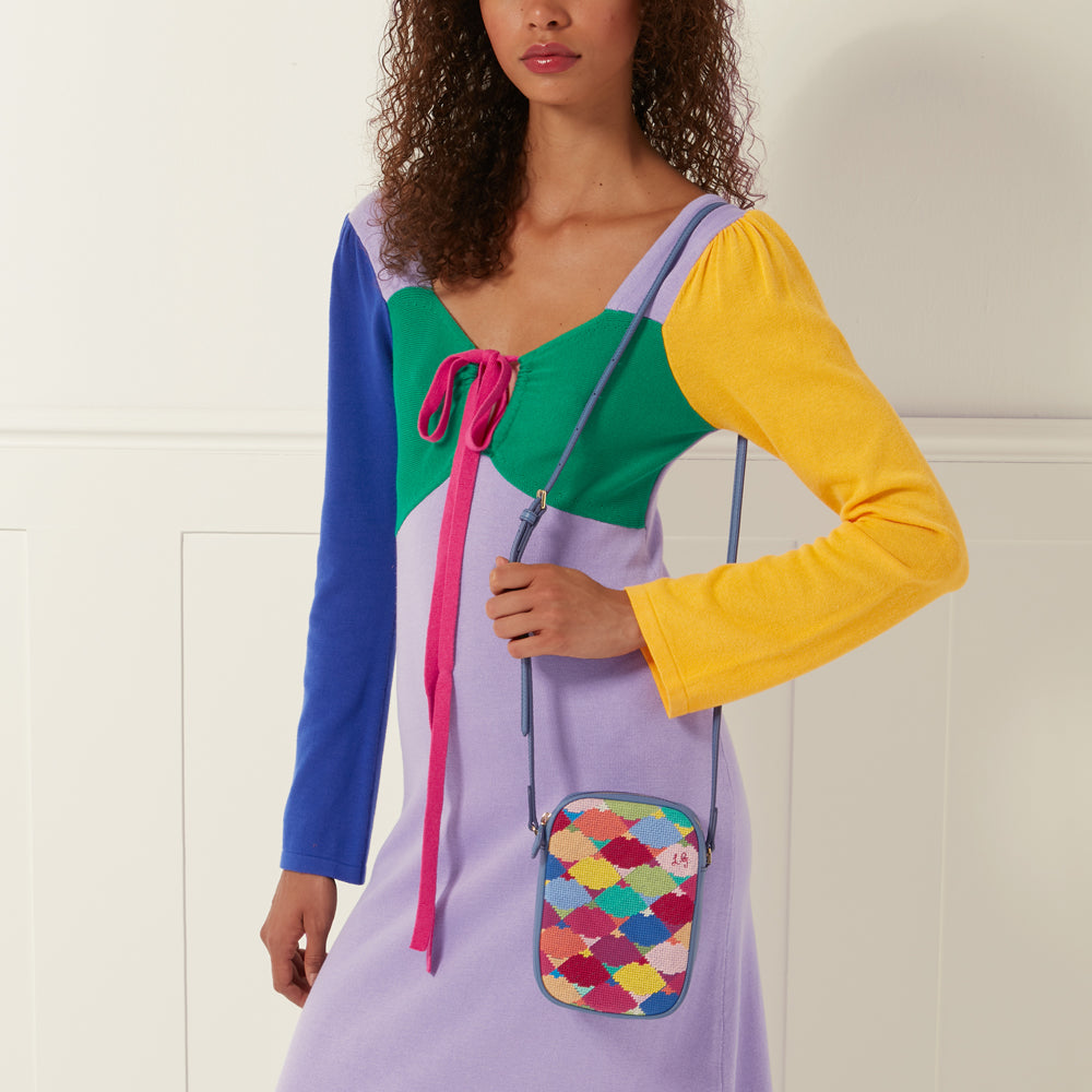 Woman in a colourful knit dress holding a small, colourful crossbody bag.