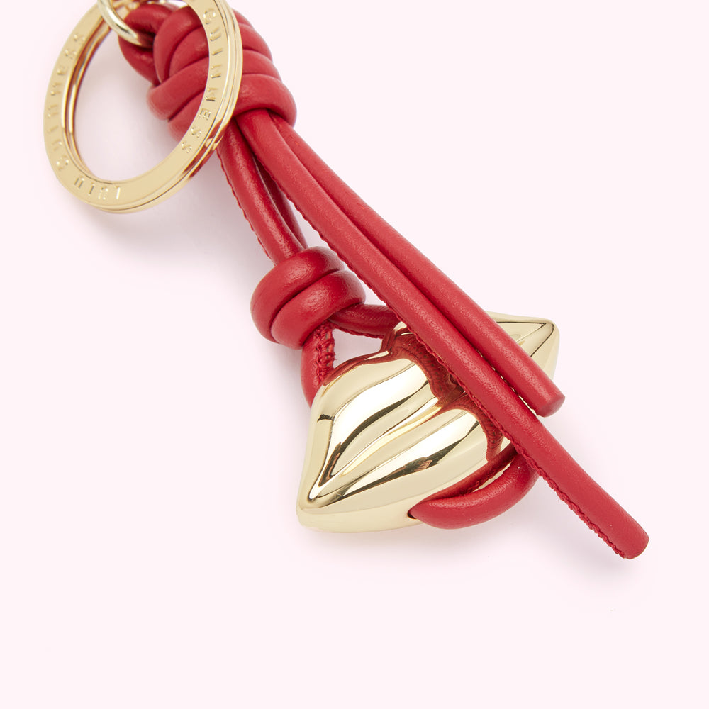 Close-up of a red leather keyring with a gold lip-shaped charm.
