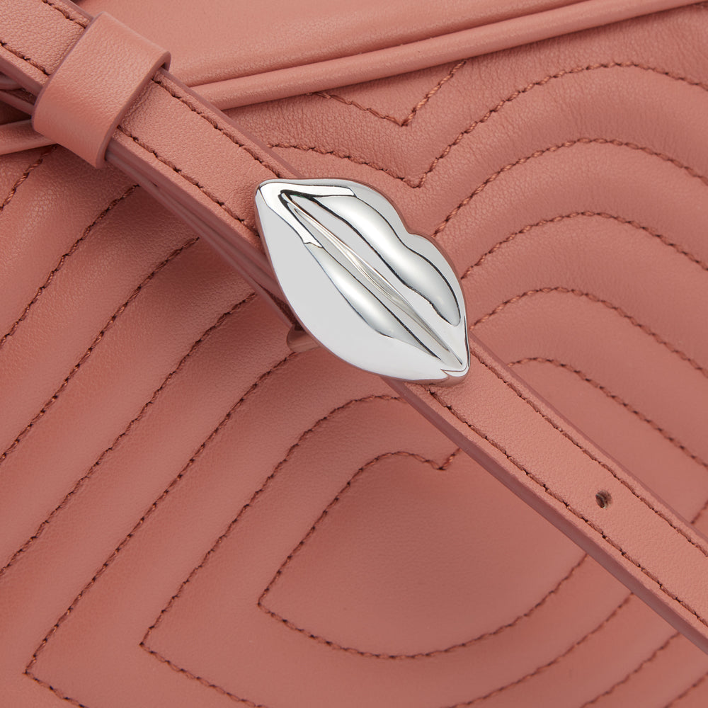 Close-up of a dusty rose quilted leather handbag with a silver lip-shaped clasp.
