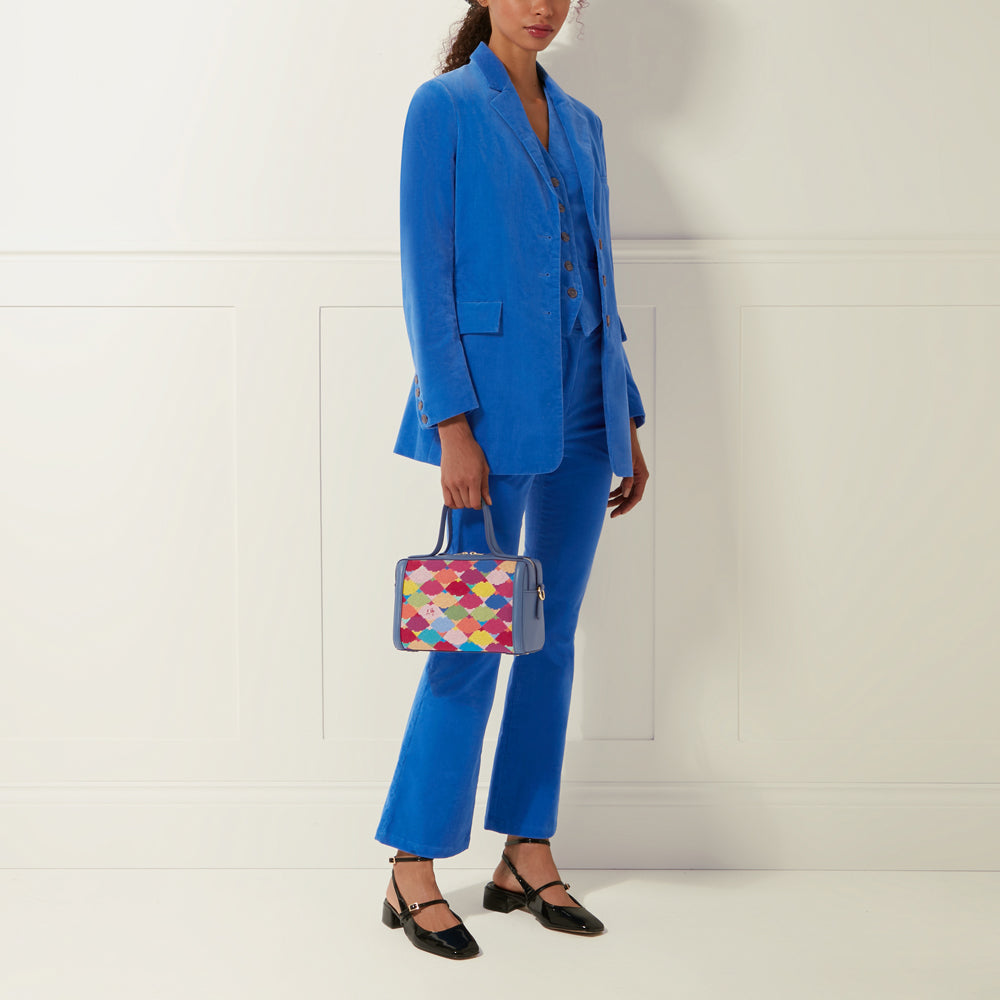 A woman in a bright blue corduroy suit carries a colourful box-shaped handbag.
