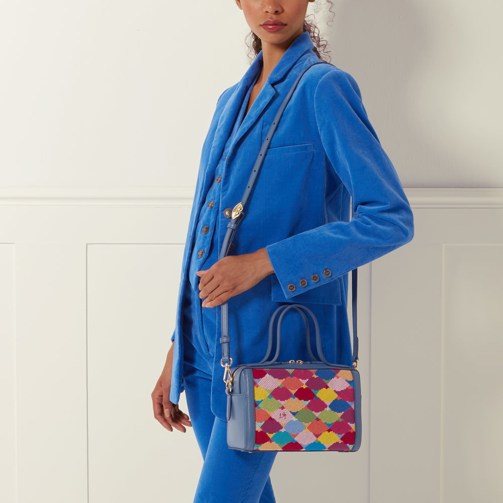Woman in a blue corduroy suit holding a blue and multi-coloured patterned handbag.
