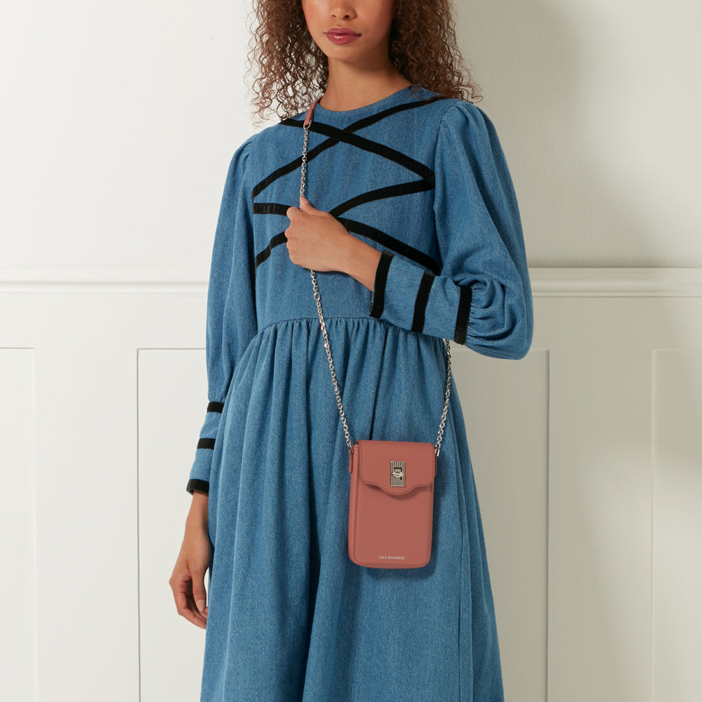 Dusty rose crossbody bag with silver chain strap on a model wearing a blue denim dress.
