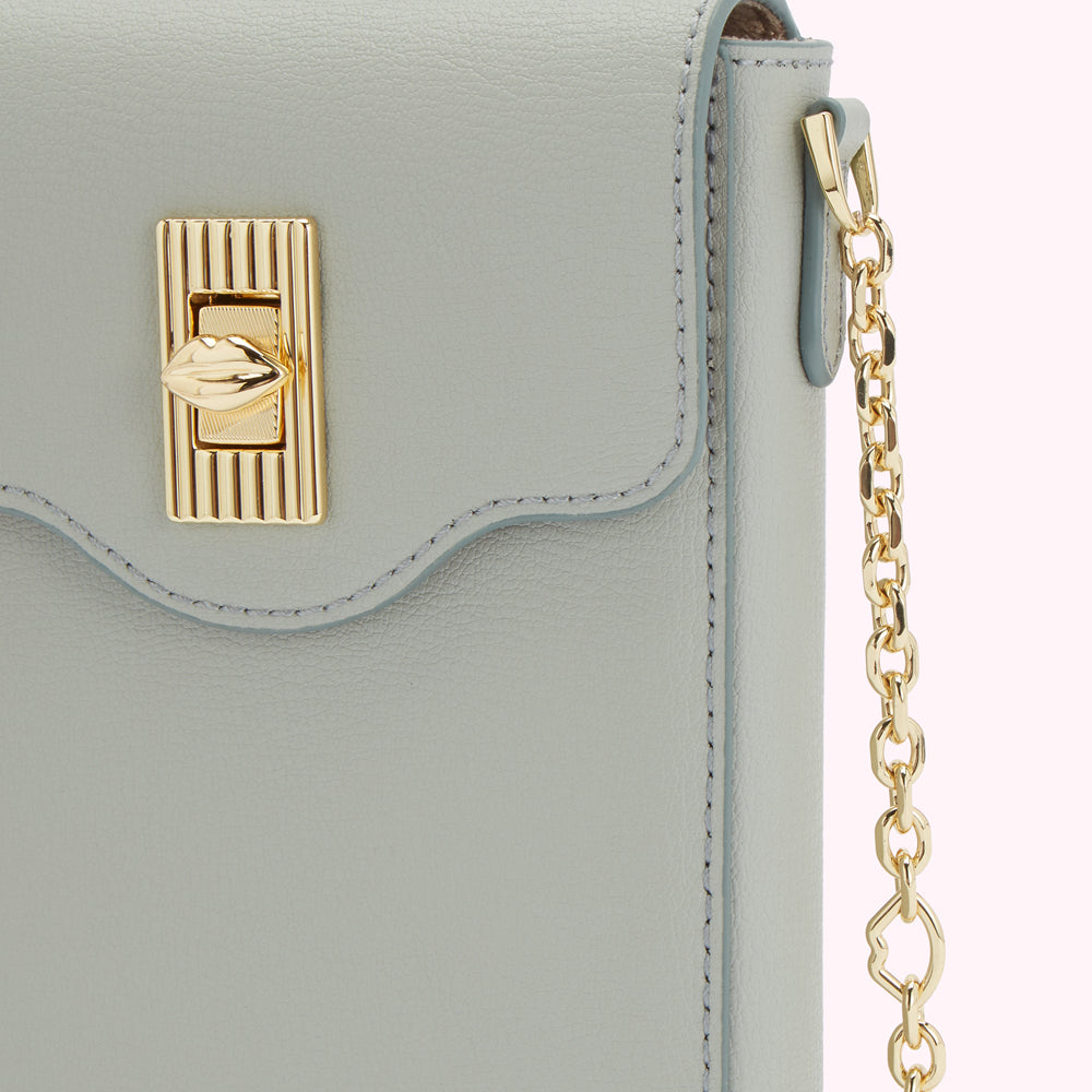 Close-up of a light grey leather handbag with a gold lip-shaped clasp and gold chain strap.
