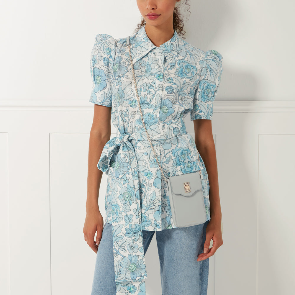 A woman wearing a light blue floral shirt dress and light blue jeans, with a light blue crossbody phone bag.
