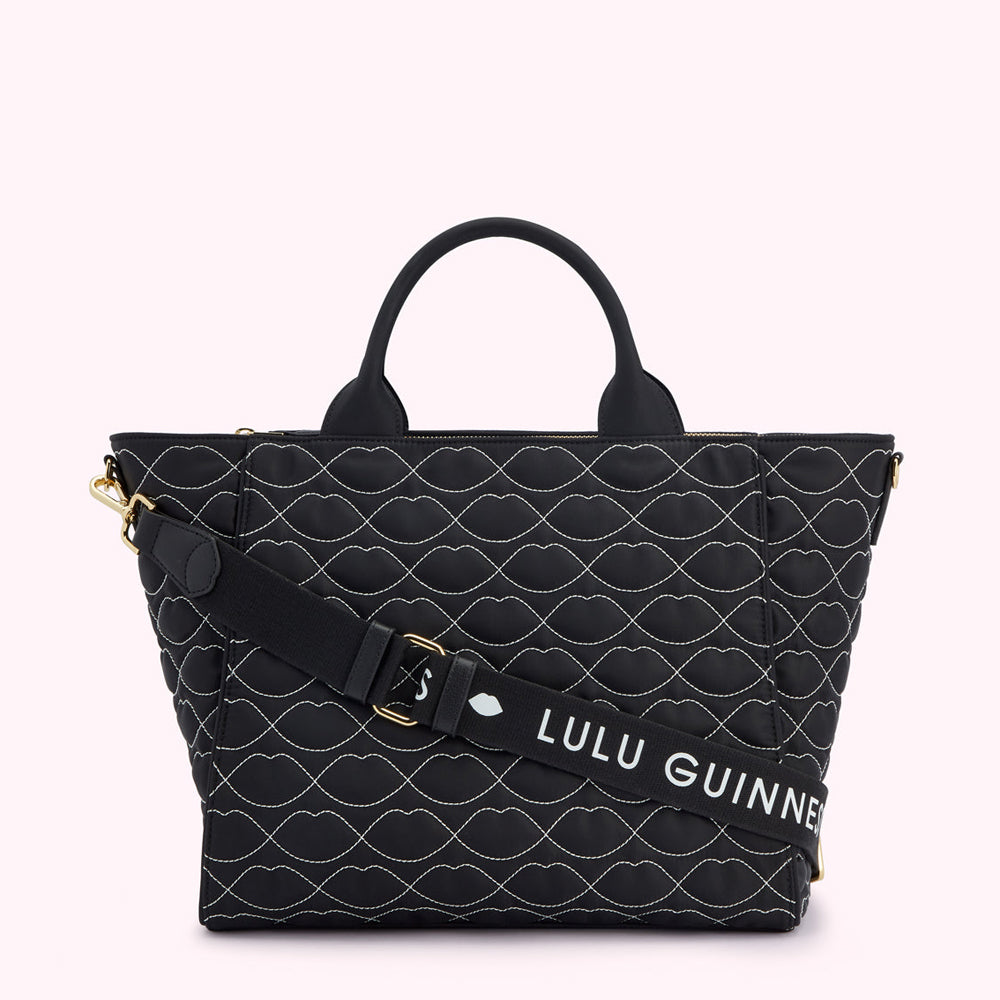 Black quilted tote bag with white lip print and detachable shoulder strap. The strap has the Lulu Guinness logo.