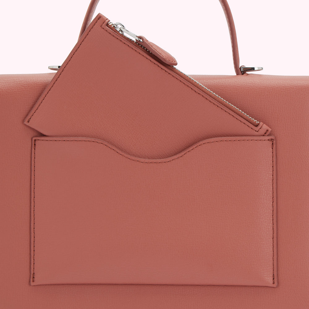Close-up of a dusty rose leather handbag with an exterior zippered pocket and a slip pocket.
