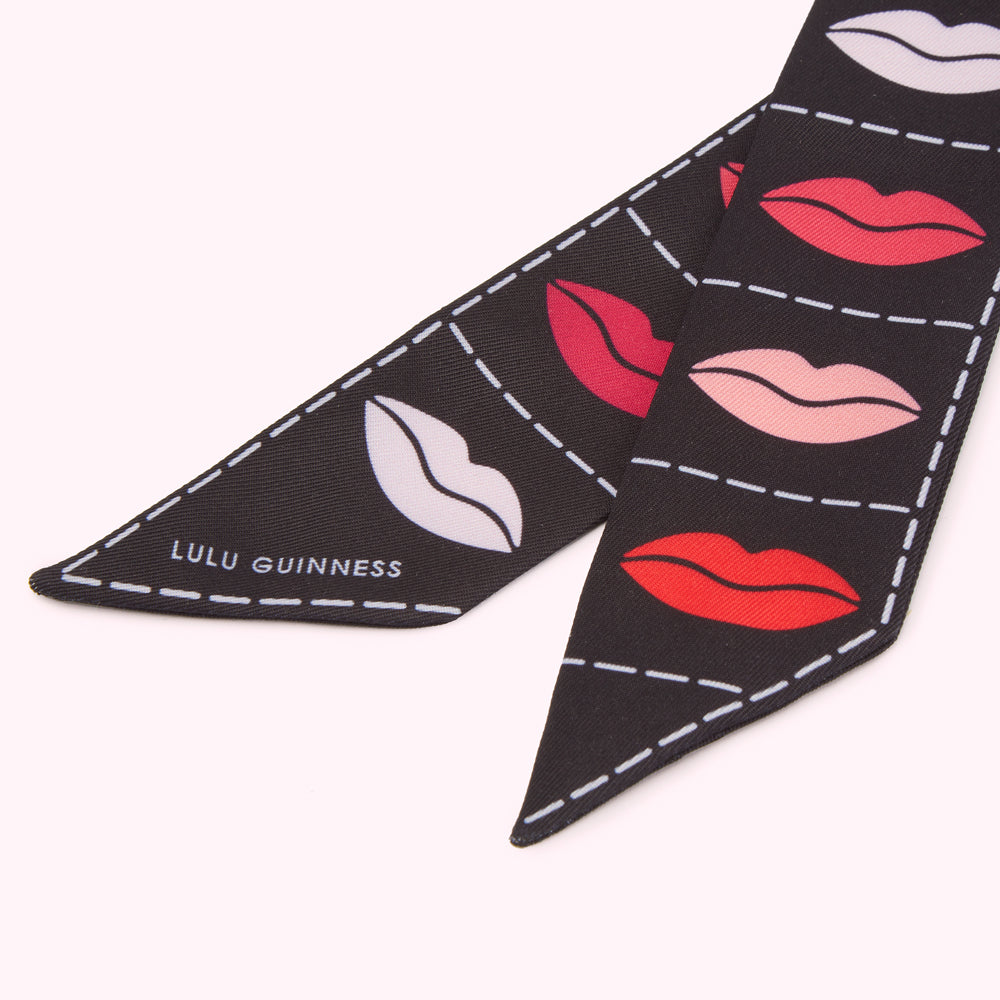 Close-up of a black Lulu Guinness scarf with a repeated pattern of lips in various colours.