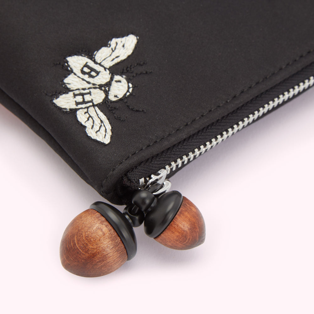 Close-up of a black pouch with an embroidered bee and wooden acorn zipper pulls.
