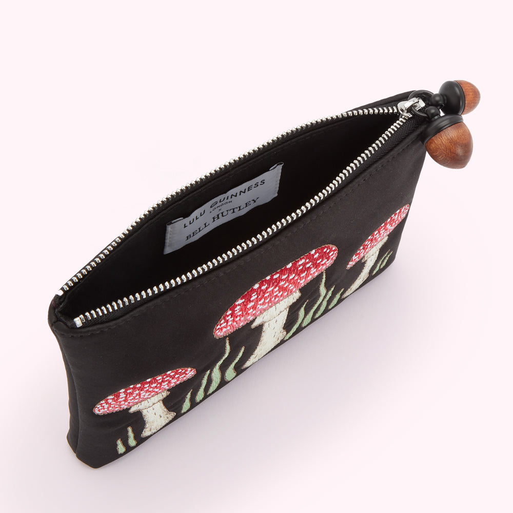 Black silk pouch embroidered with red and white mushrooms and green grass, accented with acorn zipper pulls. The inside shows a Lulu Guinness x Bell Hutley label.
