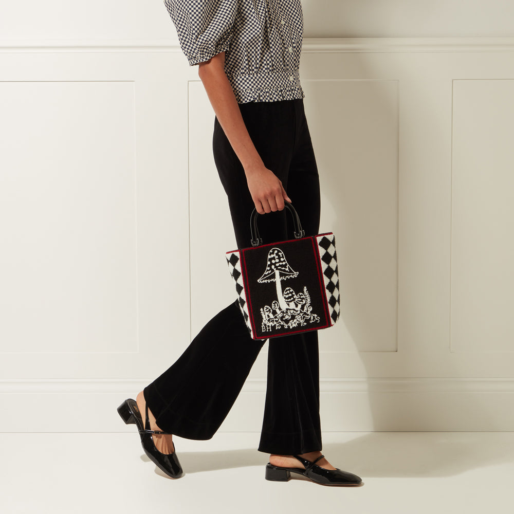 Woman carrying a black and white checkered tote bag with a mushroom design.
