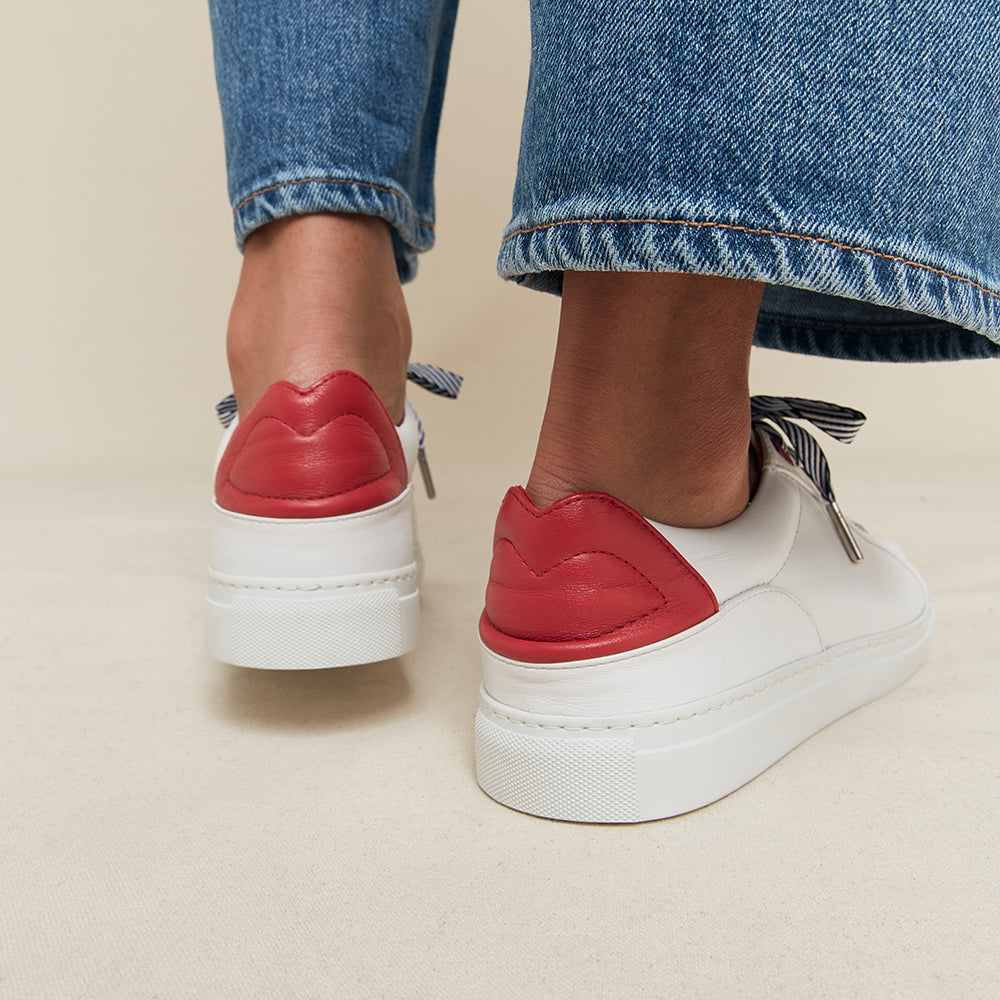 Red and white trainers with red lip details worn with blue jeans on a beige background