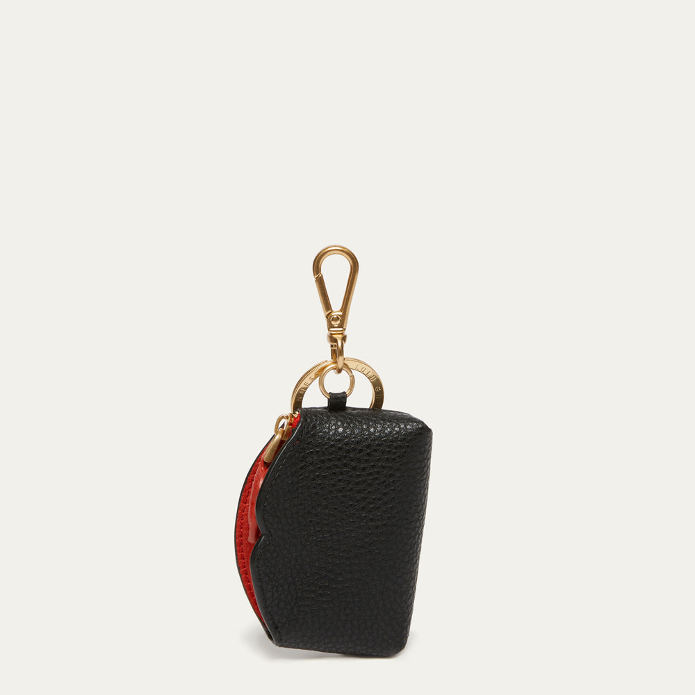 A small black pebbled leather pouch with a gold-tone lobster clasp and ring, featuring a red interior lining visible on the side, set against a light off-white background.