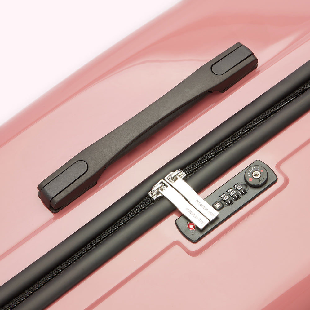 Close-up of a pink suitcase with a combination lock and handle.
