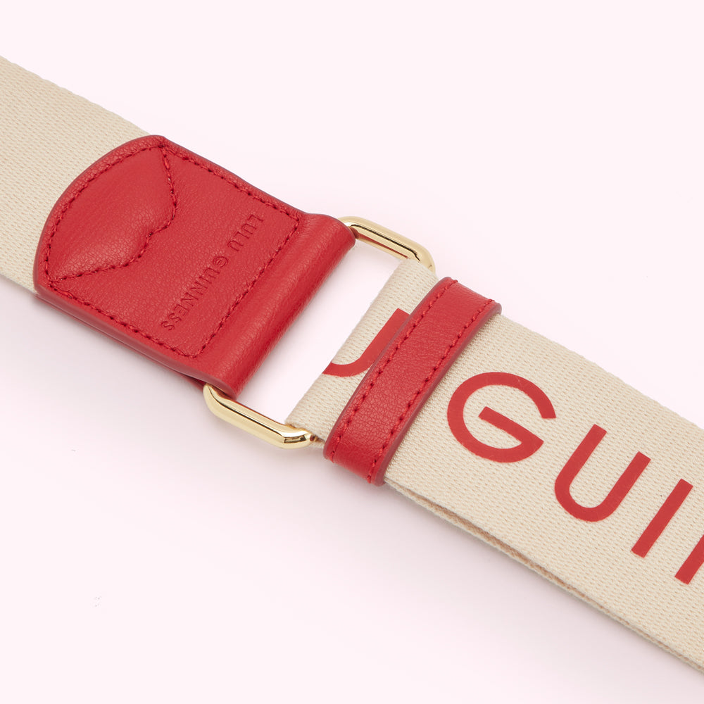 Close-up of a cream-colored bag strap with red leather detailing and the word "LULU GUINNESS" printed in red.