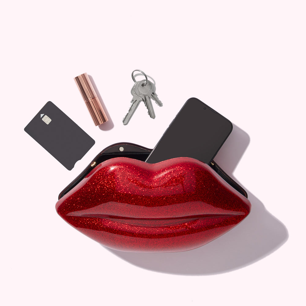 Red glitter lip-shaped purse with a smartphone, keys, credit card, and lipstick inside.

