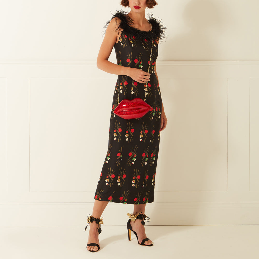 Woman in black floral dress and red lip-shaped purse.