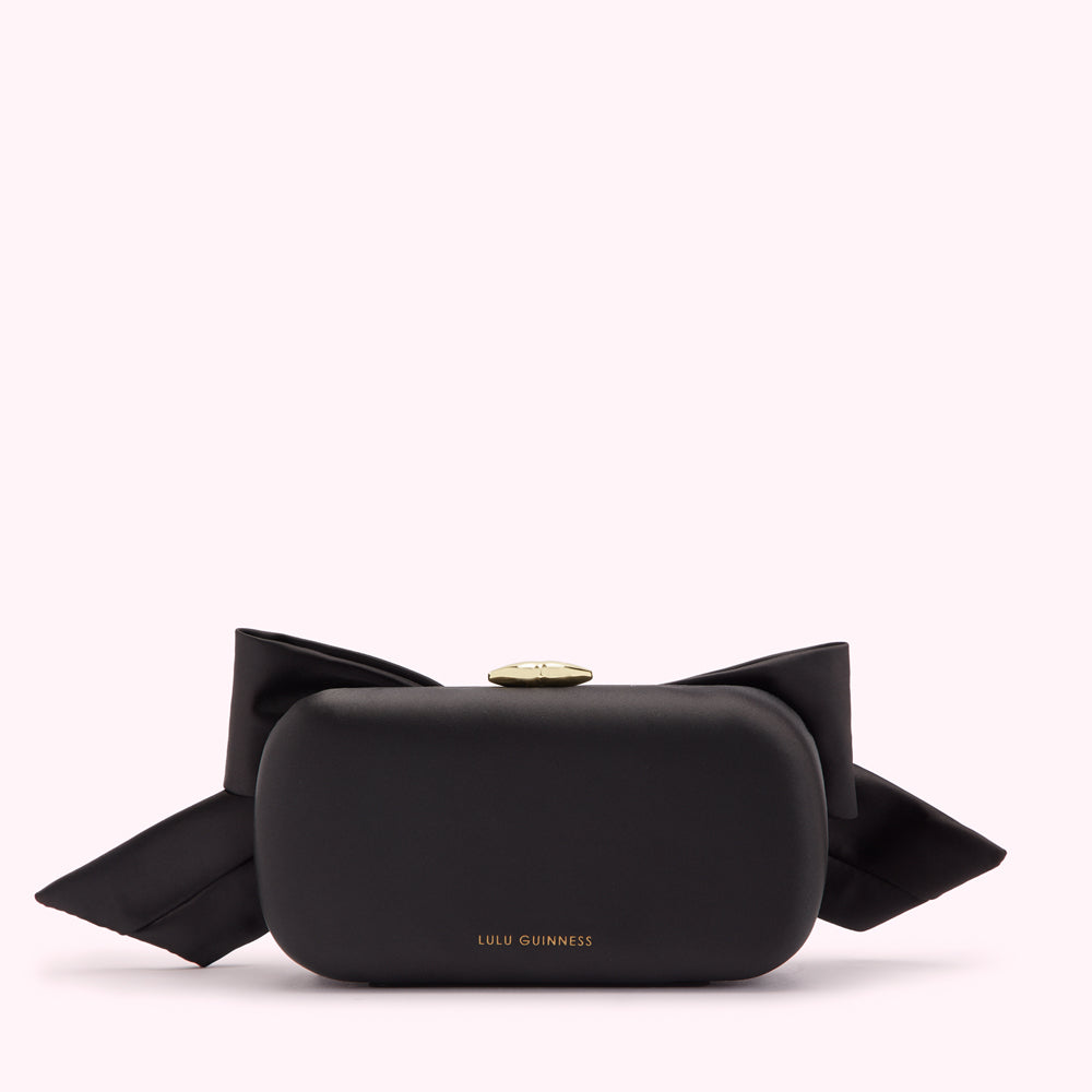 Black Lulu Guinness bow clutch bag on white background.