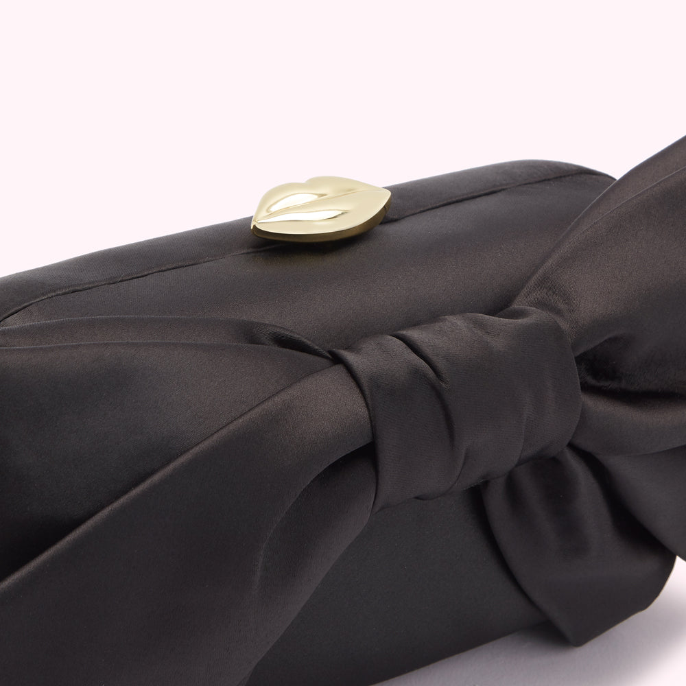 Black satin clutch with a large bow and gold lip-shaped clasp.
