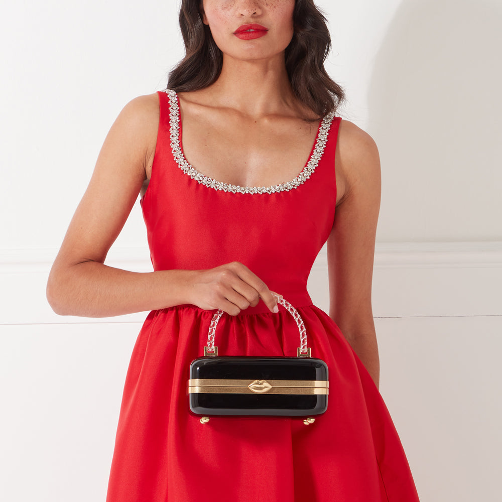 Woman in red dress holding black and gold box clutch with lip detail.