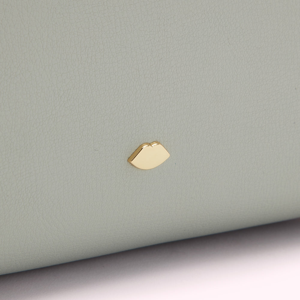 Close-up of a light grey leather item with a gold lip-shaped logo.

