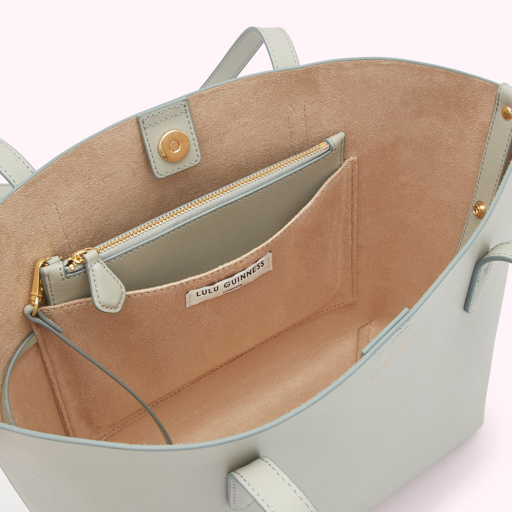 Interior of a light blue Lulu Guinness tote bag showing a beige lining, zippered pocket, and brand label.
