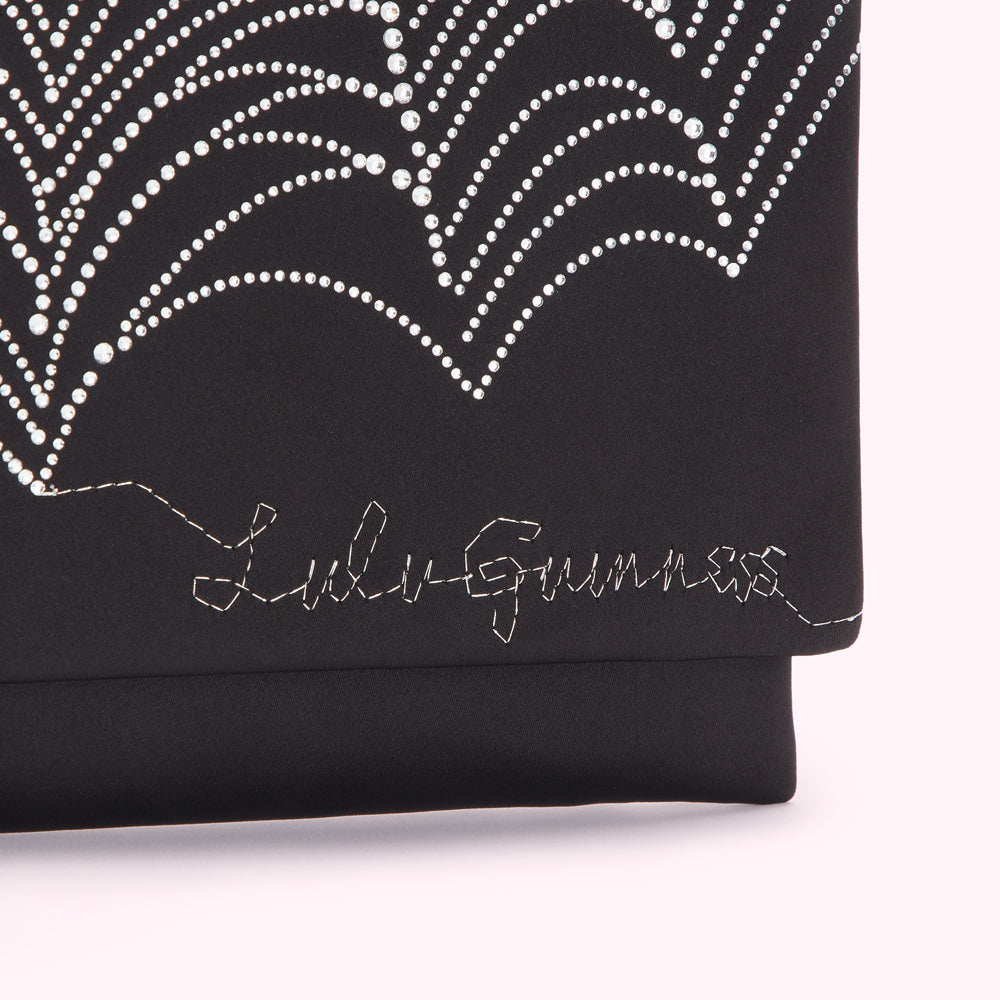 Close-up of a black Lulu Guinness clutch featuring a sparkling rhinestone design and the brand's logo stitched on the front.
