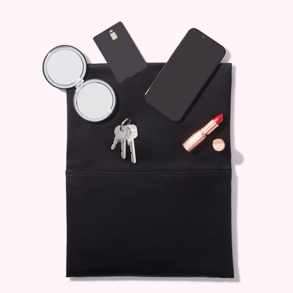 A black clutch open to reveal a smartphone, compact mirror, keys, credit card, and lipstick.