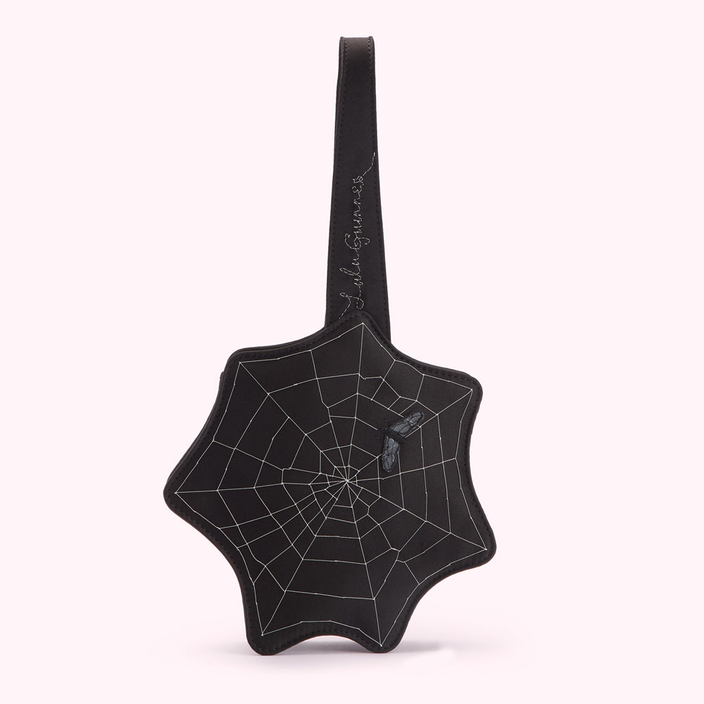 Black spiderweb-shaped bag with a small insect in the centre and a black leather strap. The designer's name is subtly stitched on the strap.
