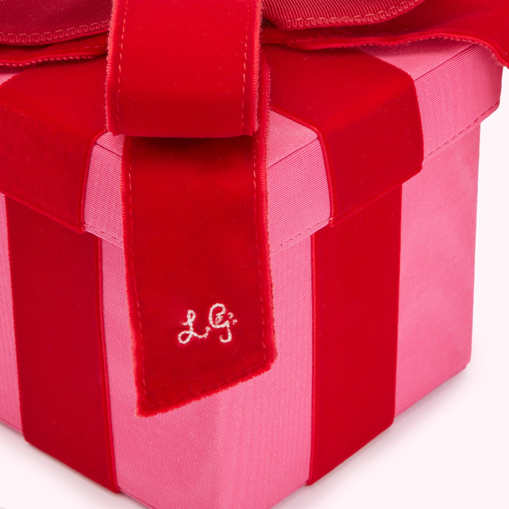 Close-up of a pink and red velvet gift box with a large red bow and the initials "LG" embroidered on the ribbon.