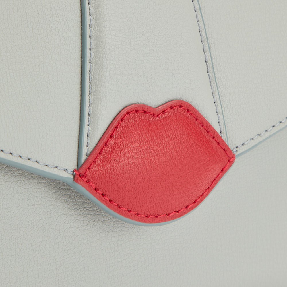 Close-up of a light grey leather bag with a red lip detail.