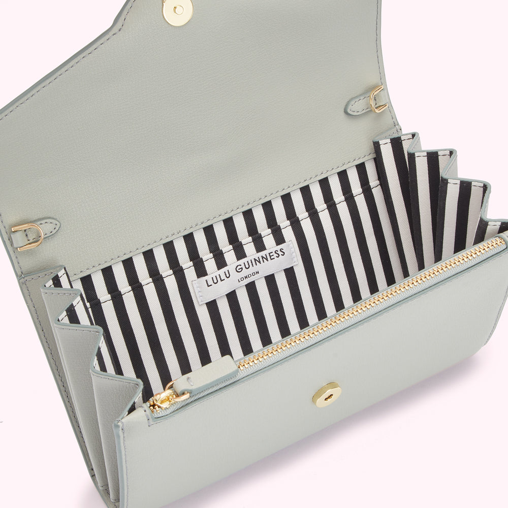 A light sage green Lulu Guinness London wallet is open to reveal its black and white striped interior.
