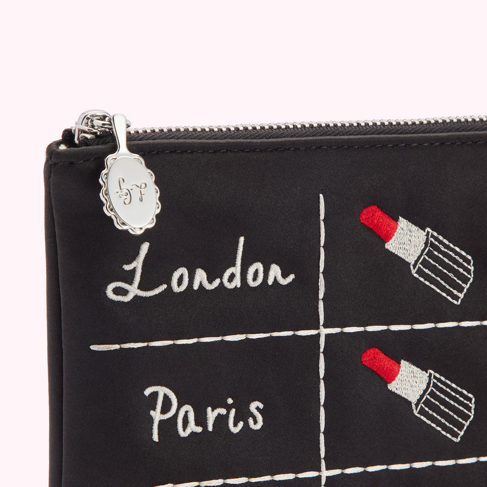 Black makeup bag with embroidered lipstick and city names; London and Paris.