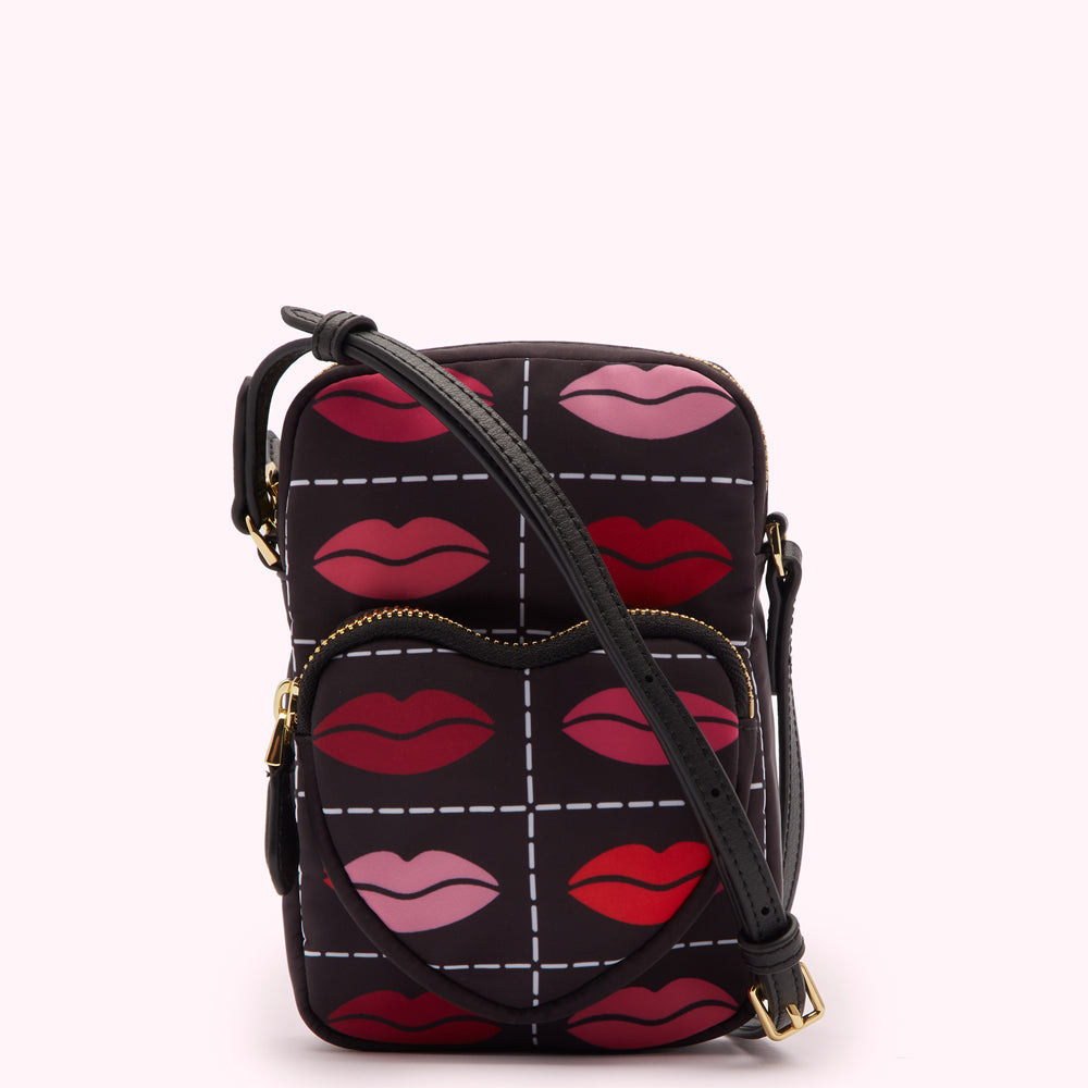 Black crossbody bag with a heart-shaped front pocket and a repeating pattern of lips in red and pink on a dark background.