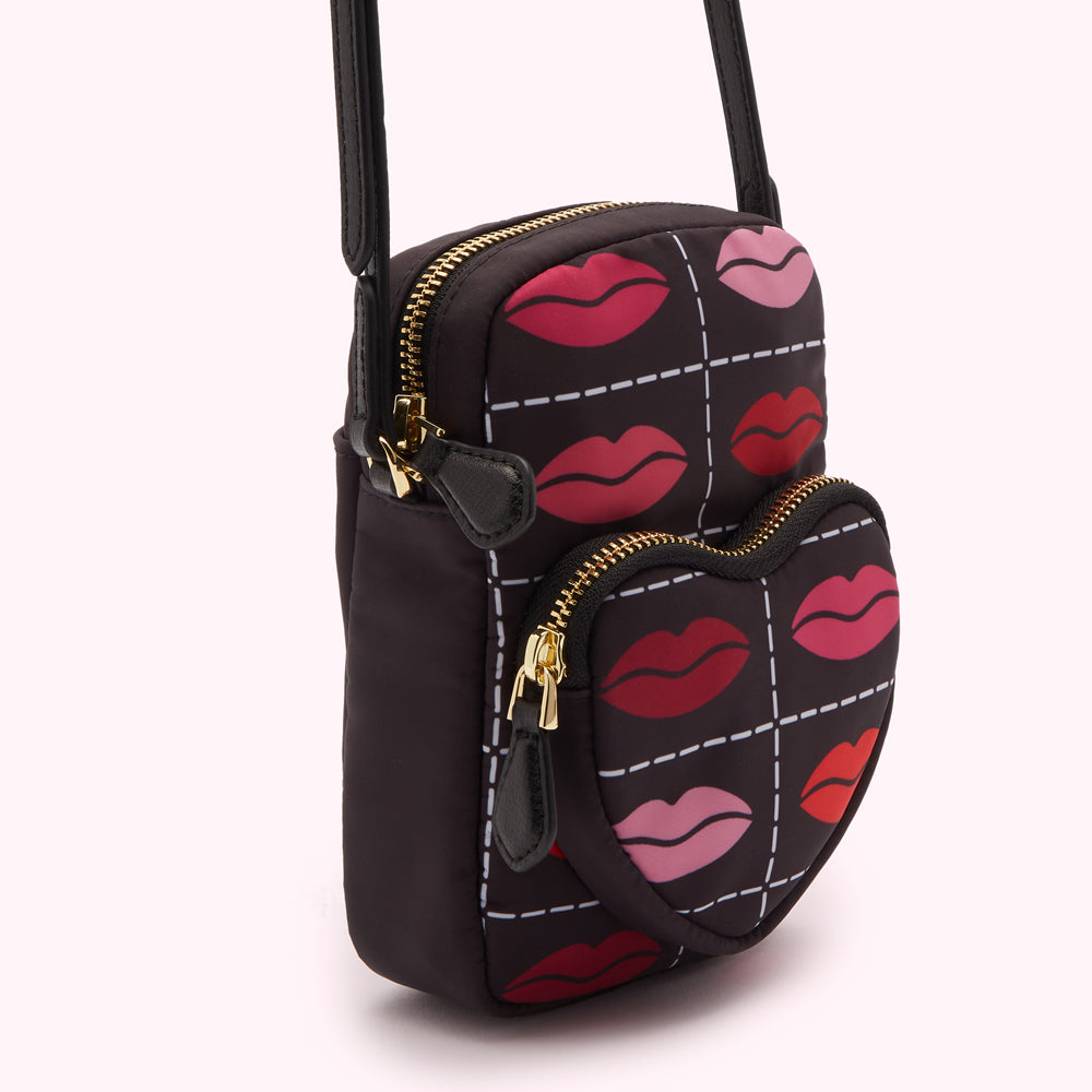 Black crossbody bag with a heart-shaped front pocket, both featuring a pattern of lips in various shades of red and pink on a black background.