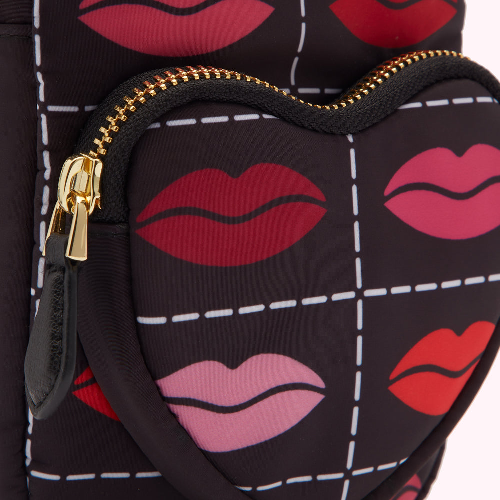 Close-up of a black heart-shaped bag with a gold zipper and a pattern of lips in various shades of red and pink.