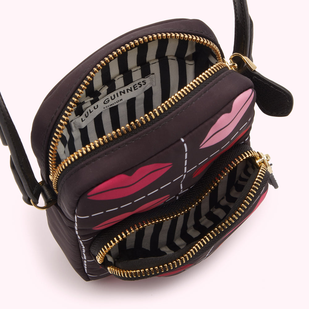 Black Lulu Guinness crossbody bag with red and pink lips print and gold zippers; the bag is open, showing a black and white striped interior.
