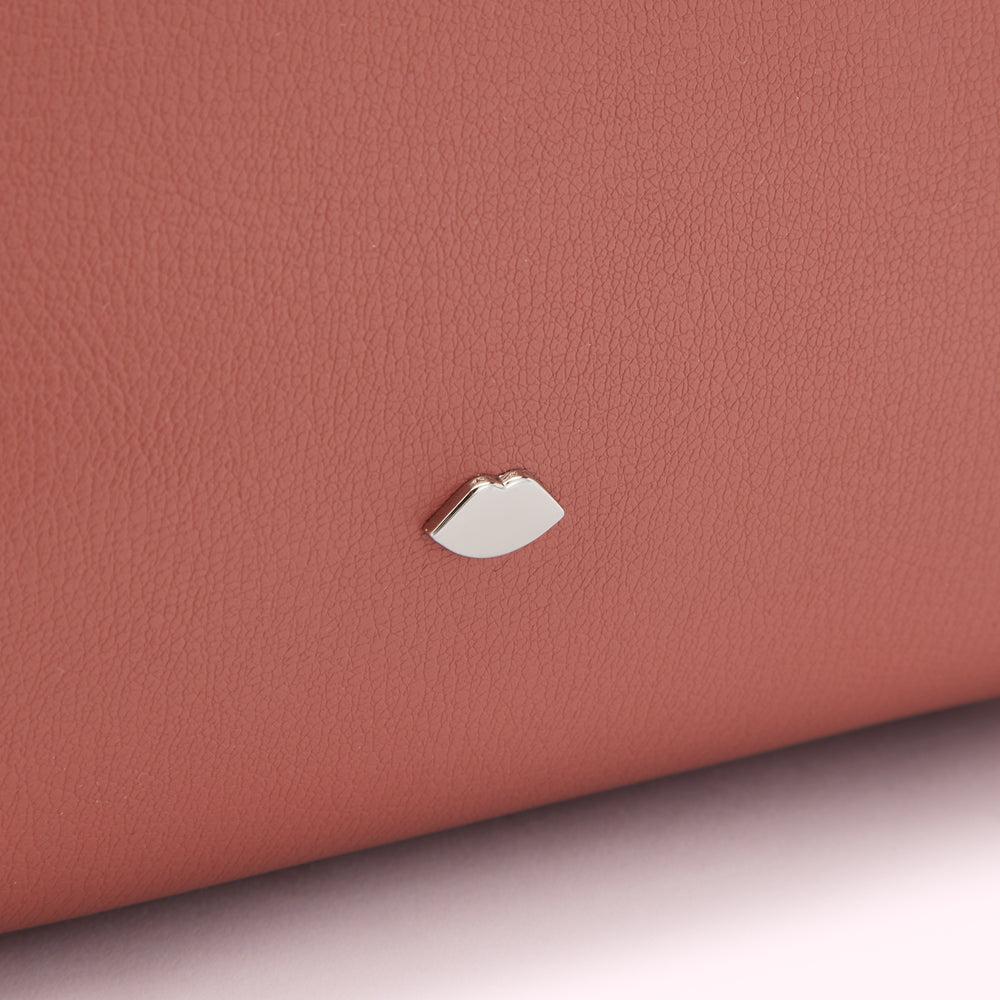 Close-up of a dusty rose-coloured leather surface with a small silver lip-shaped logo.
