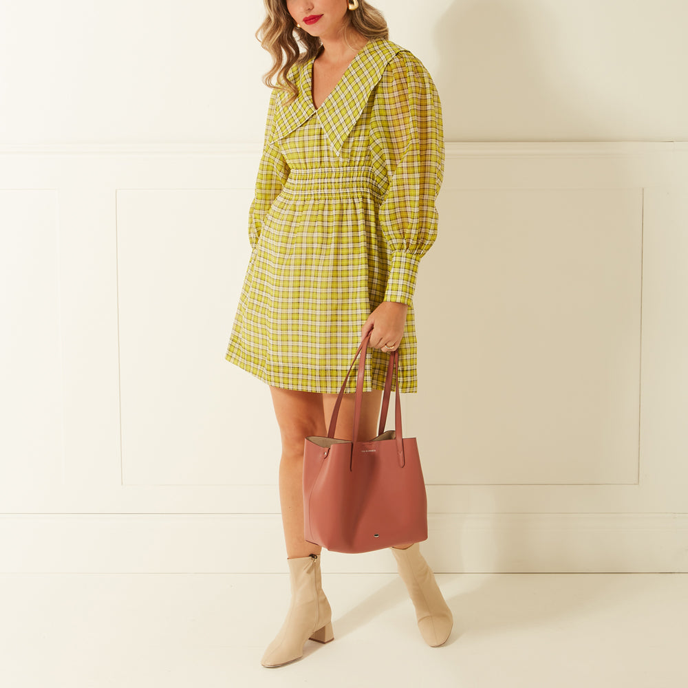 Woman in a yellow and white plaid mini dress, holding a dusty rose tote bag.
