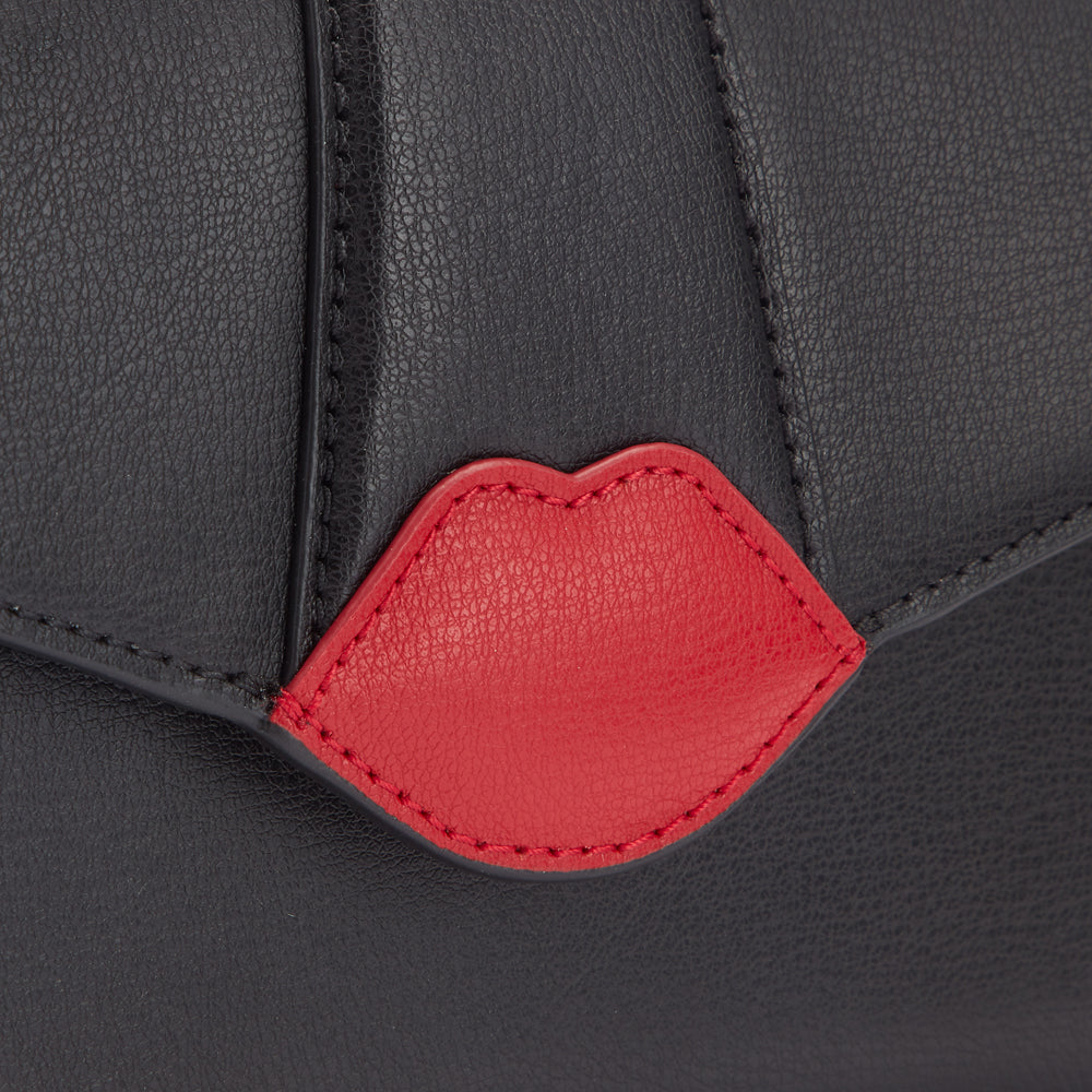 Close-up of a black leather bag with a red lip detail.
