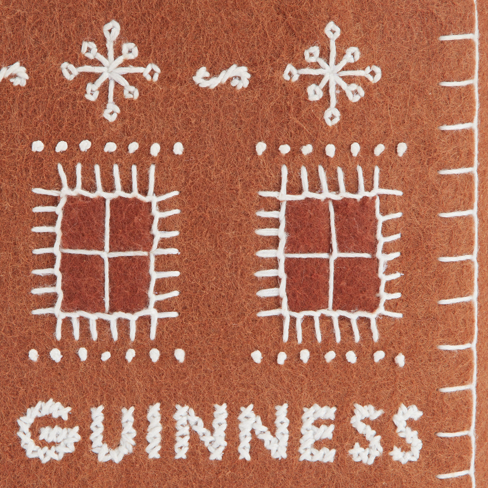 Brown felt appliqué© of a gingerbread house with the word "GUINNESS" embroidered in white thread.