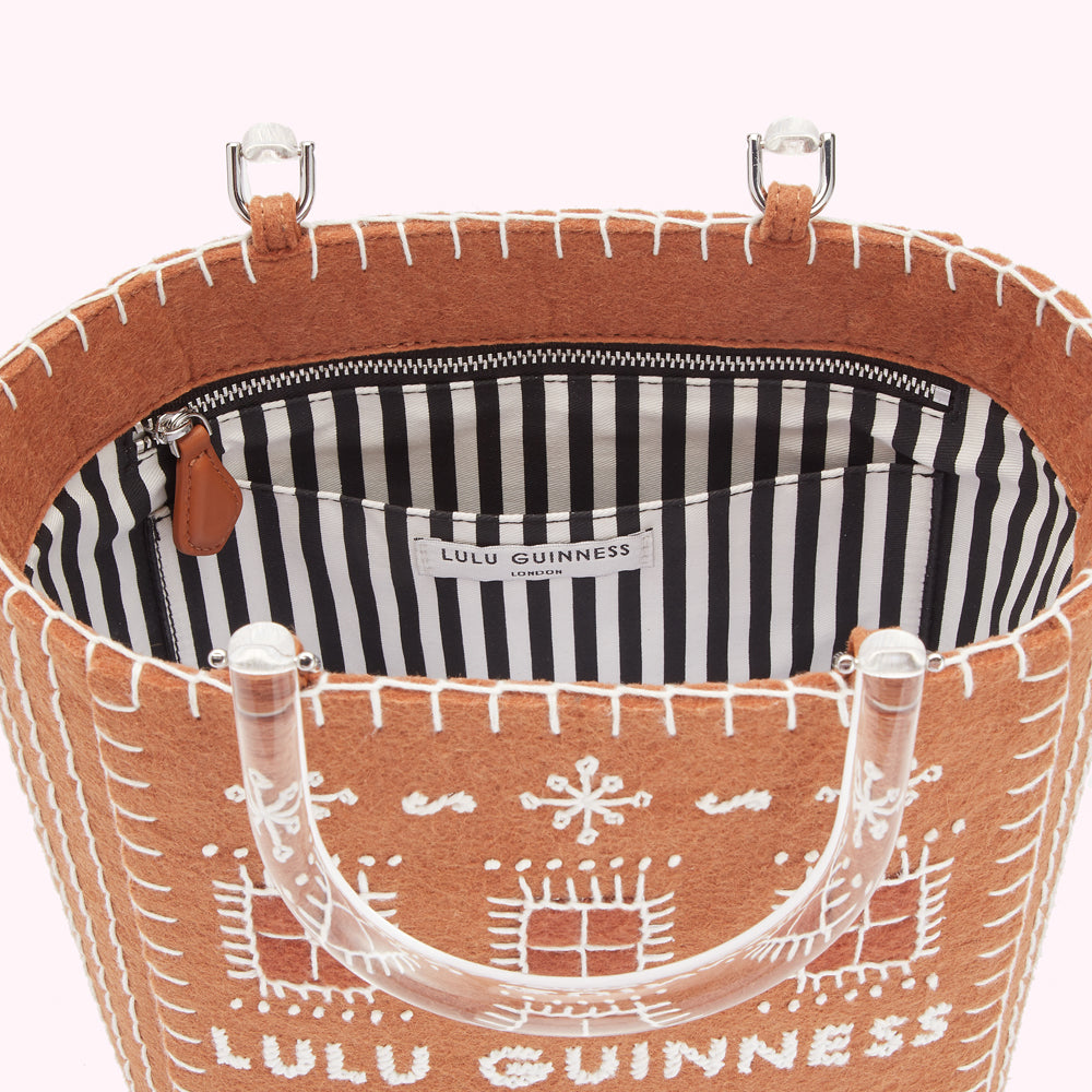 Inside view of a tan Lulu Guinness felt handbag with clear acrylic handles, featuring a black and white striped interior and white embroidered detailing.
