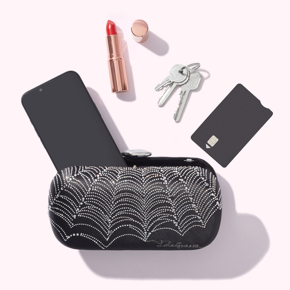 A black jewelled clutch containing a smartphone, lipstick, keys, and a credit card against a white background.