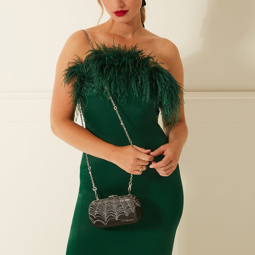 Woman in emerald green dress with feather detail and black jewelled clutch.
