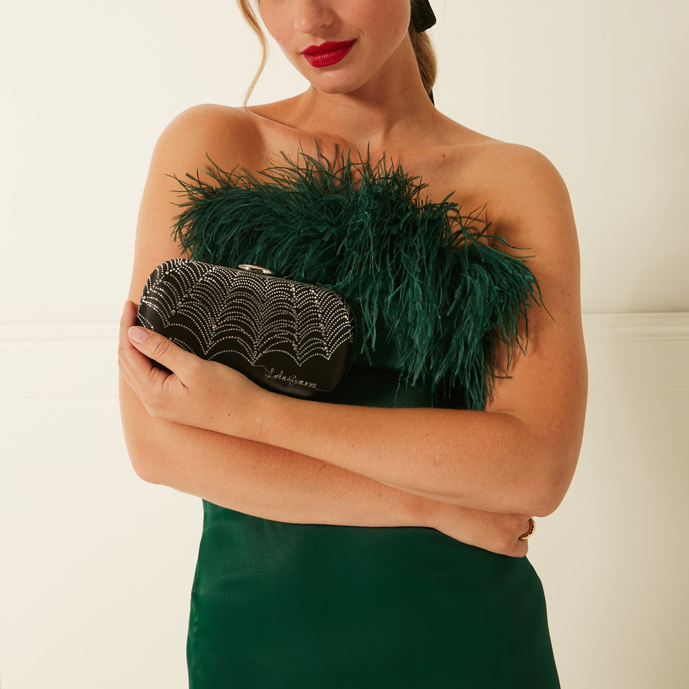 A woman in a green dress holds a black jewelled clutch.
